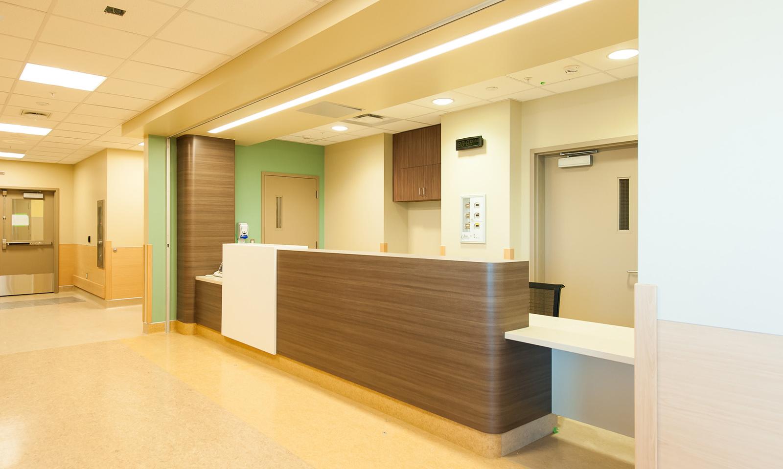 Calgary South Health. Reception desk with brown wood laminate and rounded corners. Pale green accent wall.