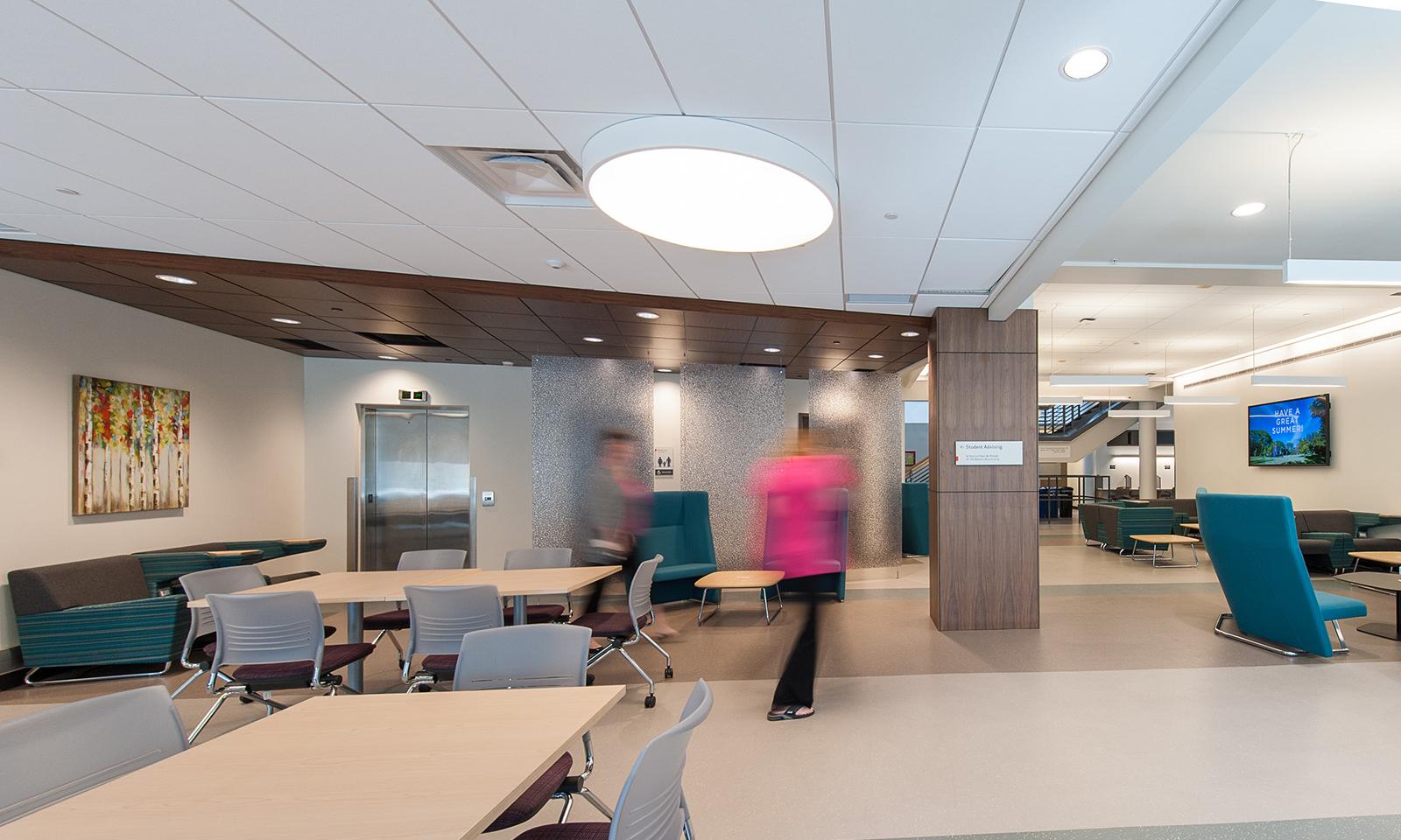 University of Calgary School of Nursing. General use area with white tables, grey chairs and additional soft seating. 