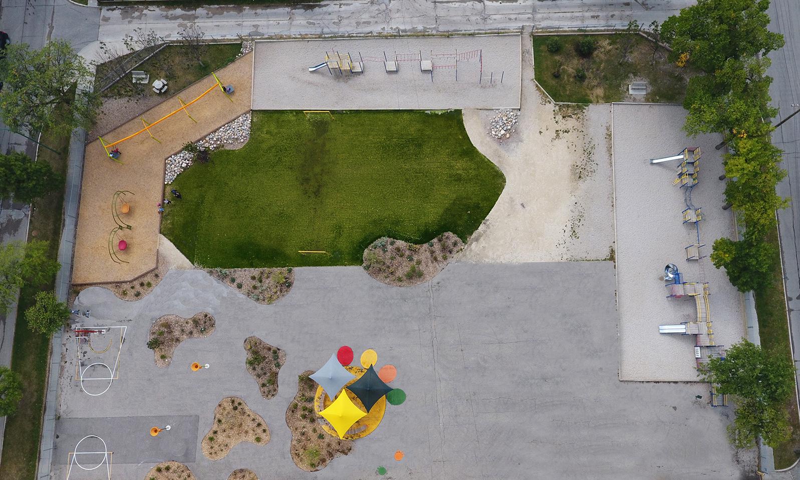 Ecole Provencher Schoolyard. An aerial view of the entire schoolyard including a green space, slides, plantings, umbrellas and seating area, hopscotch, and tarmac.