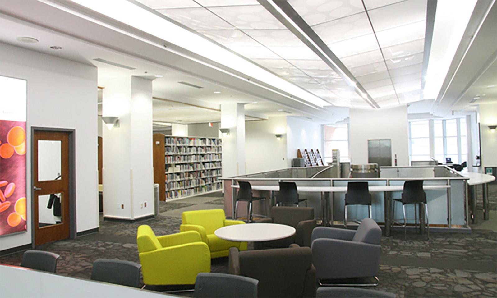 University of Manitoba, Neil John Maclean Library. Open study space with a variety of seating in a spacious open area and book stacks in the background.